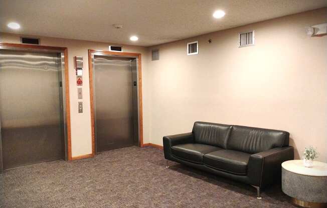 A black leather couch sits in a room with a carpeted floor and two elevators.