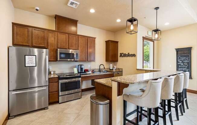 A kitchen with a refrigerator, microwave, oven, and bar stools.