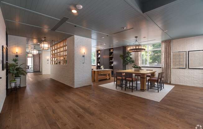 View of the resident lounge with white brick walls, square wooden table with cognac colored chairs and wooden floors  at Sylvan Uptown, Denver