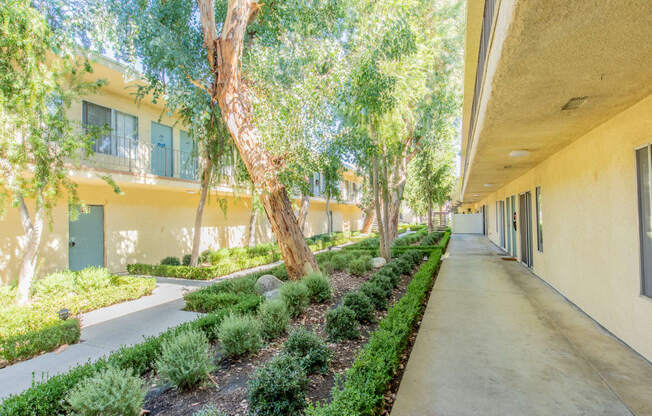 a long corridor with trees and bushes next to a building