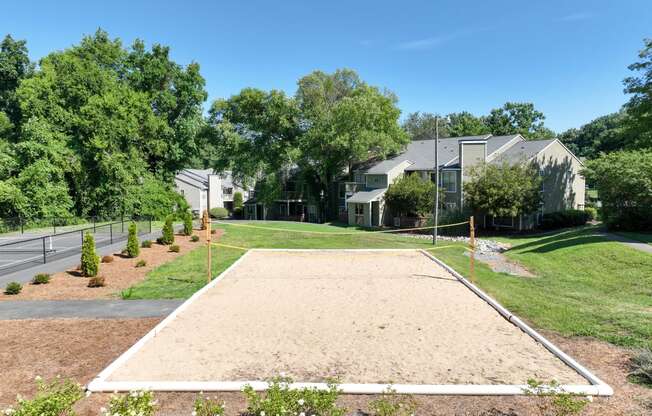 the yard has a sandy volleyball court with a house in the background