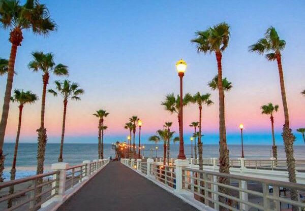 a pier with palm trees and the ocean at sunset