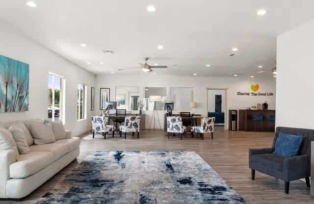 A spacious living room with a rug in the center and a sign that says "Sharing the Good Life".