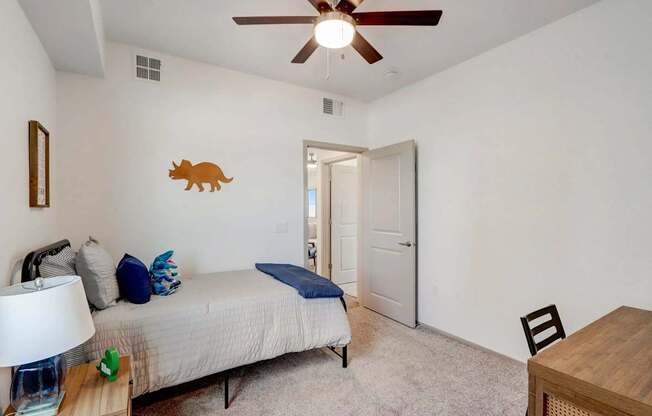 A bedroom with a bed, a ceiling fan, and a wooden table.