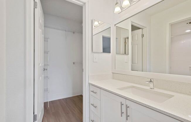 Bathroom with cabinets, sink, mirror, medicine cabinet, and lighting looking into walk-in closet