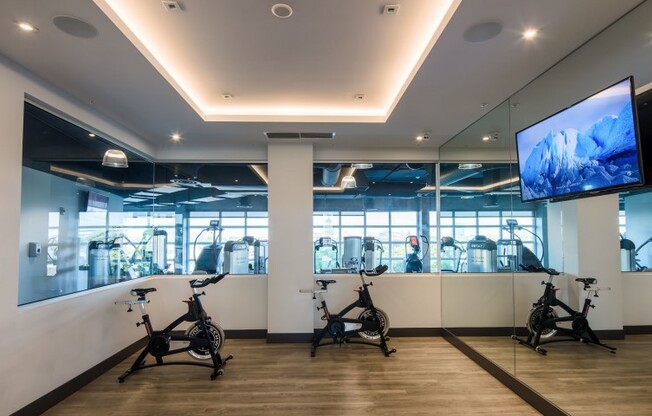 The fitness center at our apartments in Miami, featuring spin bikes facing a TV and a view of the work out room & gym