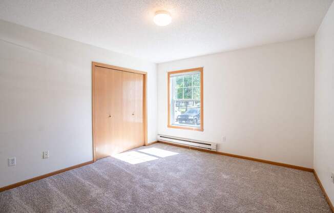 A bedroom with a carpeted floor, a door, a window. Fargo, ND Stonebridge Apartments