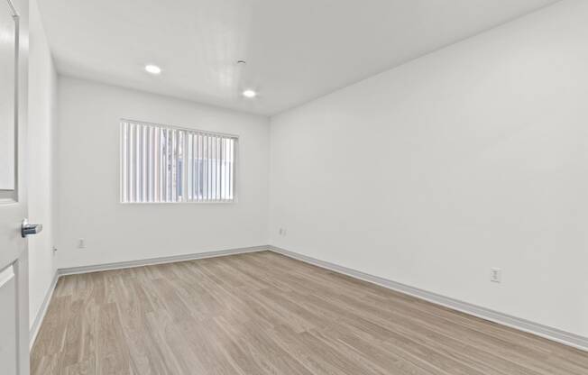 a living room with white walls and wood floors and a window