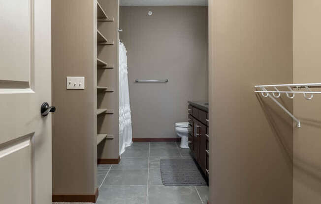 A walk-in closet with a carpeted floor and that leads into bathroom
