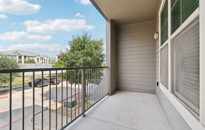 A balcony with a metal railing overlooks a parking lot and houses.