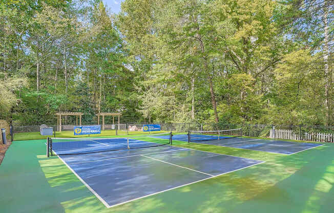A tennis court surrounded by trees and a fence.