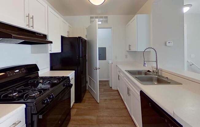 A kitchen with black appliances and white countertops and wood-style floors.