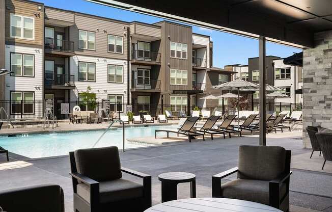 A poolside area with chairs and tables in front of apartment buildings.