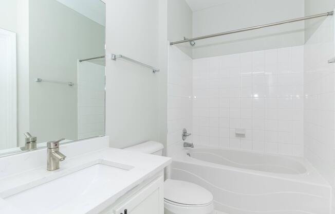 Modern bathroom featuring a white tiled shower and tub combination, a sleek sink with a faucet, a mirror above the sink, and a minimalistic design. The walls are painted in a light color, and there are chrome fixtures for a clean and polished look.