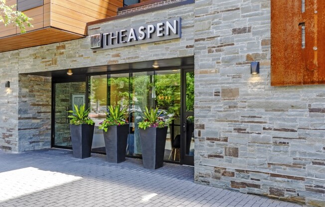 The exterior of The Aspen apartment community, featuring sliding glass doors and a stone masonry facade.