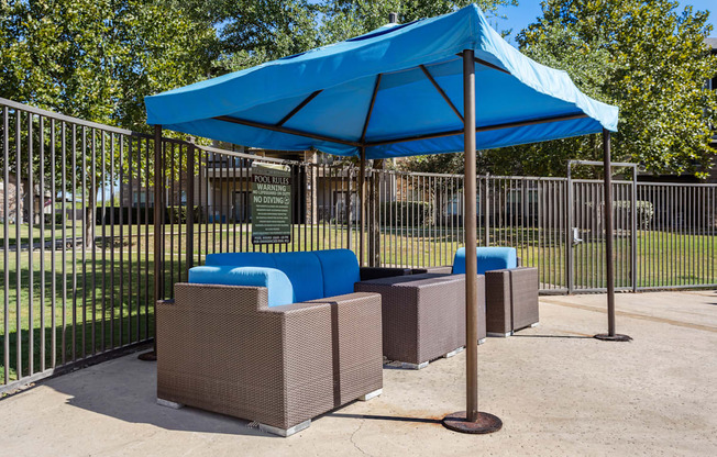 a blue umbrella and three couches in front of a fence