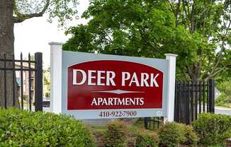 A sign for Deer Park Apartments is displayed in front of a fence and greenery.
