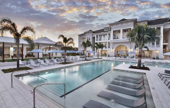 a large swimming pool with chaise lounge chairs and umbrellas in front of a large