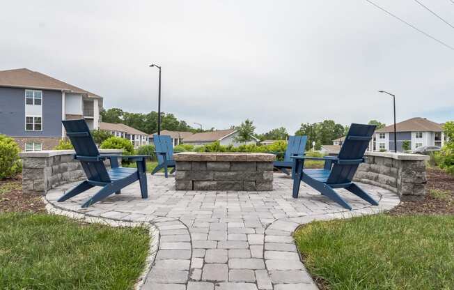 a stone patio with blue chairs and a stone fire pit