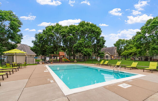 A large outdoor swimming pool surrounded by trees and lounge chairs.