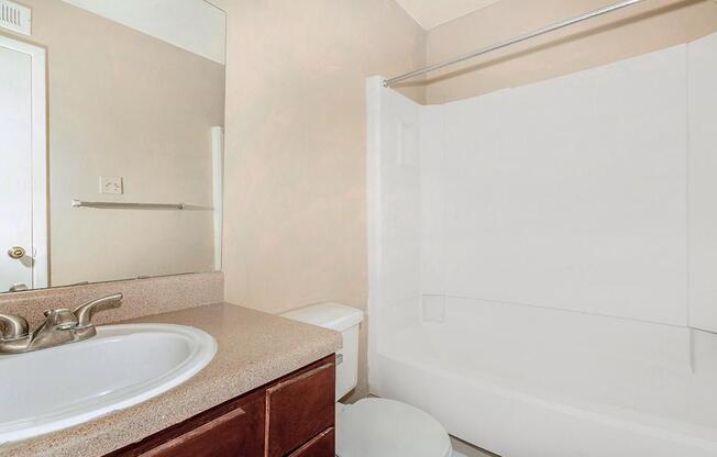 A clean and modern bathroom featuring a sink with a countertop, a mirror above the sink, a toilet, and a bathtub with an adjoining shower. The walls are painted light beige, and the flooring is not visible. A towel bar is mounted on the wall. The overall ambiance is bright and inviting.