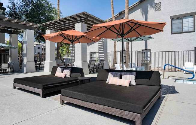 Two cushioned daybeds are placed under umbrellas on a patio. at Lazo Apartment Homes, Chandler, AZ