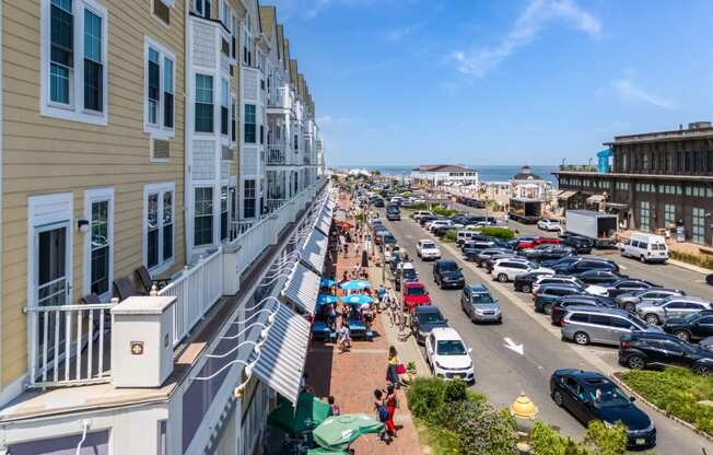 A street view of a sunny day with cars parked on the side of the road and people walking on the sidewalk.