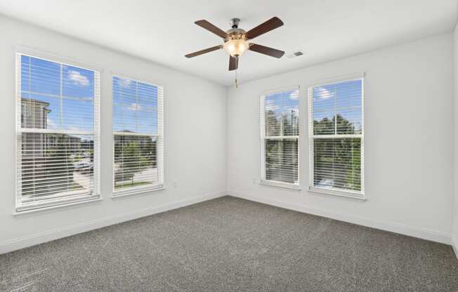 an empty living room with three windows and a ceiling fan