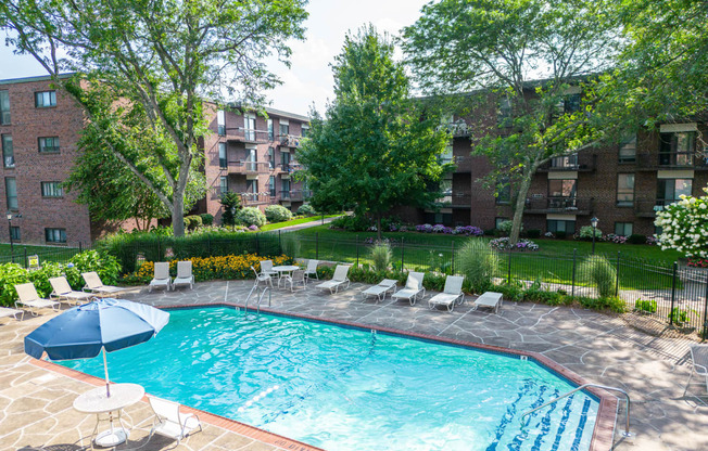 a swimming pool with chairs and an umbrella in front of an apartment building