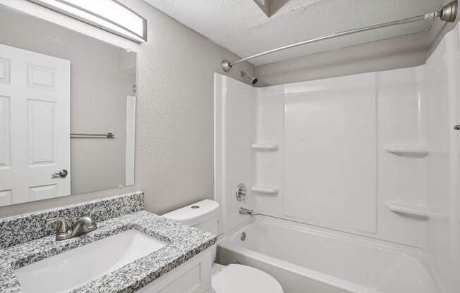 A white bathroom with a granite countertop and a white bathtub.