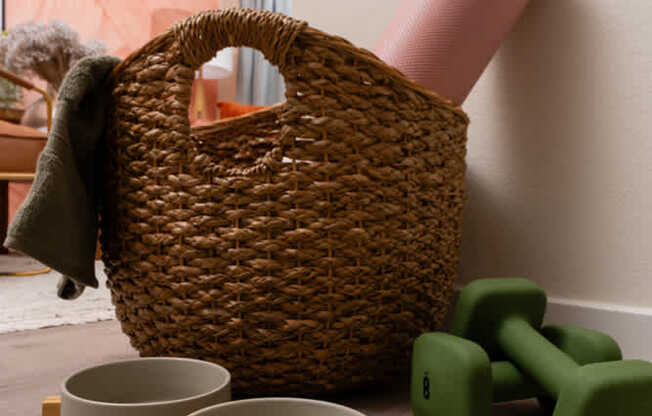 A wicker basket sits on a wooden stand with two bowls and two green dumbbells in the foreground.
