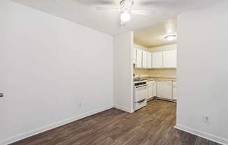 the living room and kitchen of an apartment with white walls and wood flooring