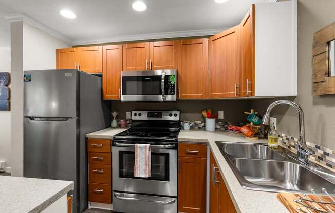 A kitchen with a stove, oven, refrigerator, microwave, and sink.