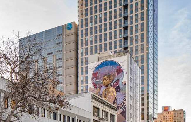 A tall building with a blue top stands next to a building with a mural on it.
