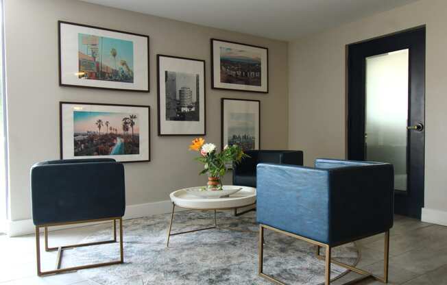 a living room with blue chairs and a table and pictures on the wall