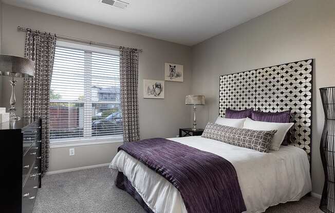 City Place at Westport - Fully Furnished Bedroom With Cozy Bed, Dresser, Carpet Flooring, and a Window With Blinds and Curtains