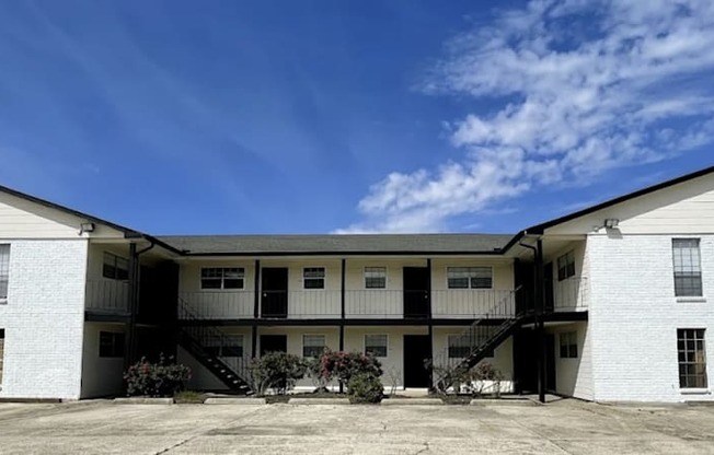 A white two-story building with a flat roof and a balcony on the second floor.