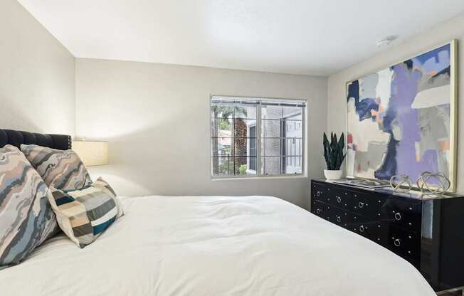 A bedroom with a bed, dresser, and a painting on the wall.