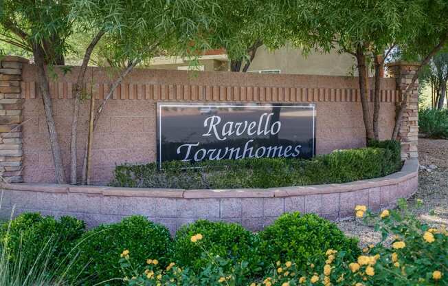 A sign that says Ravello Townhomes is surrounded by plants and trees.