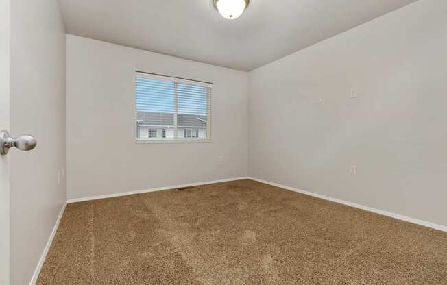 A room with a carpeted floor and a window with blinds.
