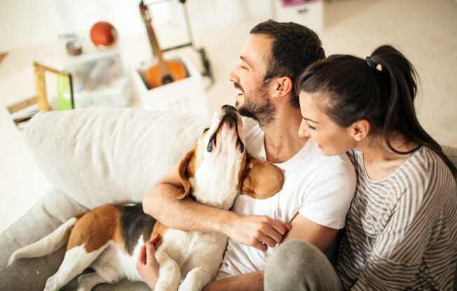 a man and woman sitting on a couch playing with a dog