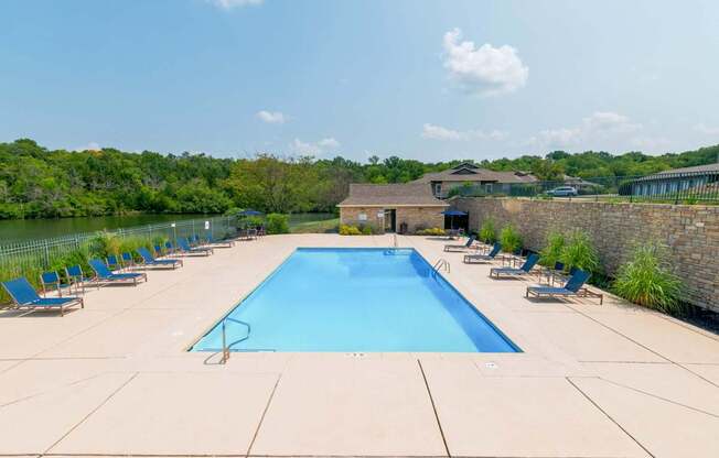 A large swimming pool surrounded by lounge chairs and a stone wall.