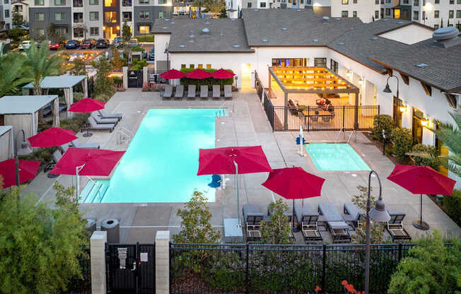 A pool surrounded by red umbrellas and chairs.