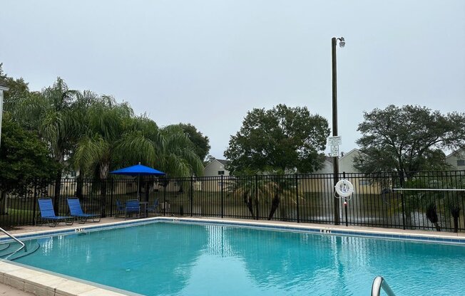 A pool with a blue umbrella and a black fence.