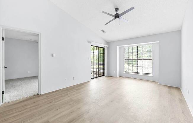A spacious room with a ceiling fan and a sliding glass door leading to a balcony.