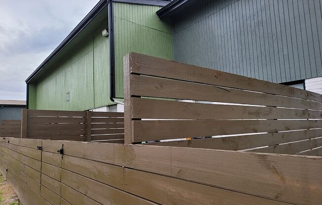 a fence with wooden boards in front of a green building at Ivy Plains at Brooks Apartments, Texas, 78223