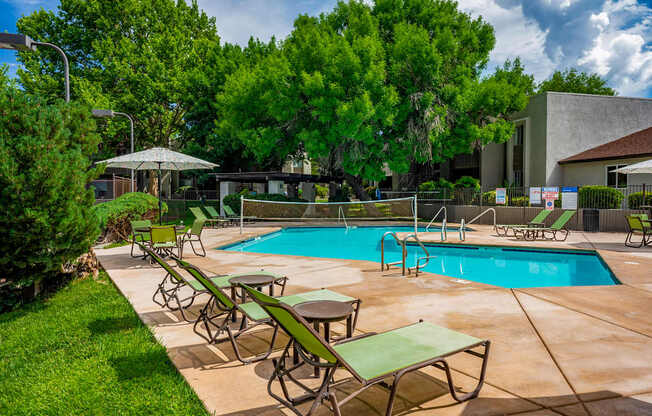 A pool surrounded by green lawn chairs and trees.