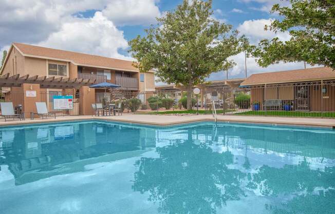 A swimming pool in front of a building with a blue sky and clouds in the background.