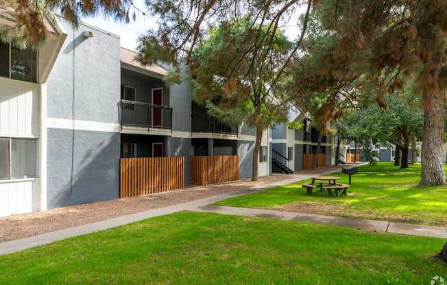 A building with a red door and a balcony is surrounded by trees and a picnic table.