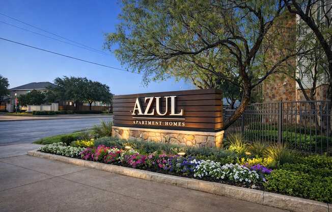 A sign that says "AZUL Apartment Homes" is lit up at dusk.